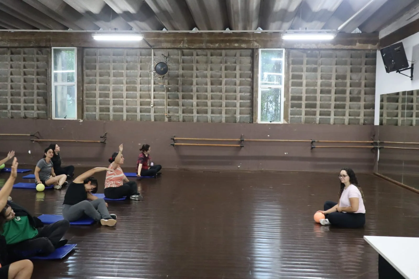 Aula coletiva em estúdio Pilates, idosos sentados em colchonetes.